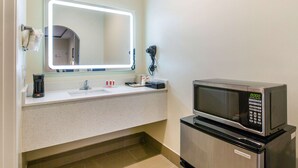 A bathroom with a sink, a mirror with lights, a hairdryer, and a microwave. - Econo Lodge Inn & Suites Houston Willowbrook (Houston)