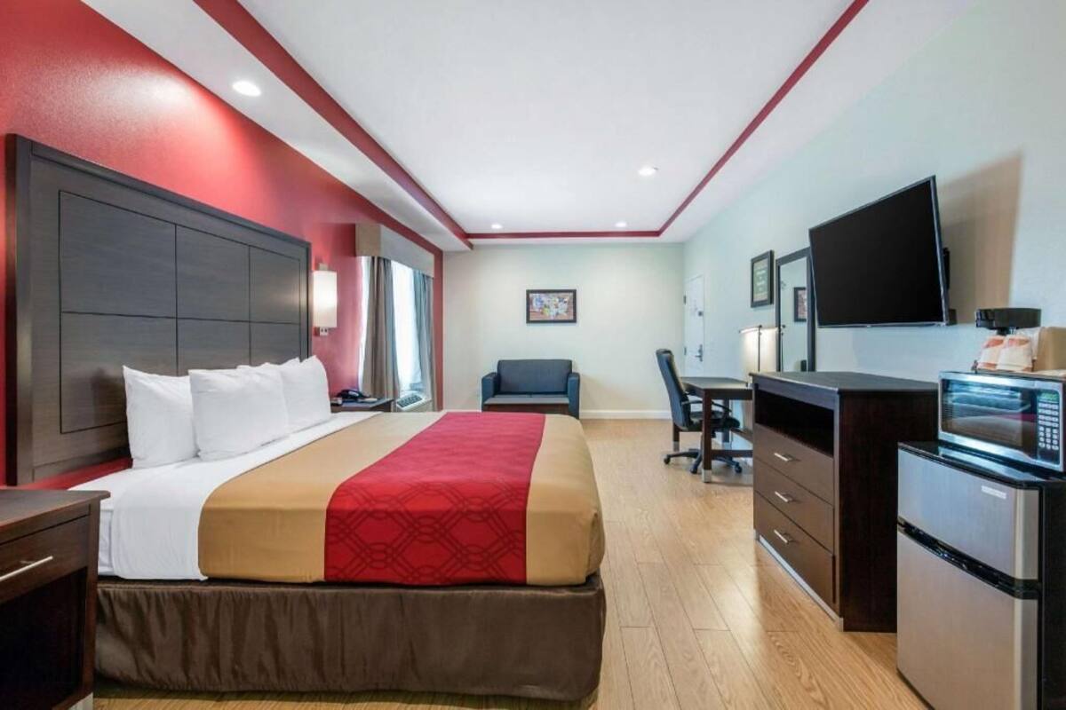 A hotel room with a bed, desk, chair, TV, and kitchenette.