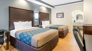 A hotel room with two beds, a desk, a chair, and a bathroom visible through an archway. - Econo Lodge Inn & Suites Houston Willowbrook (Houston)