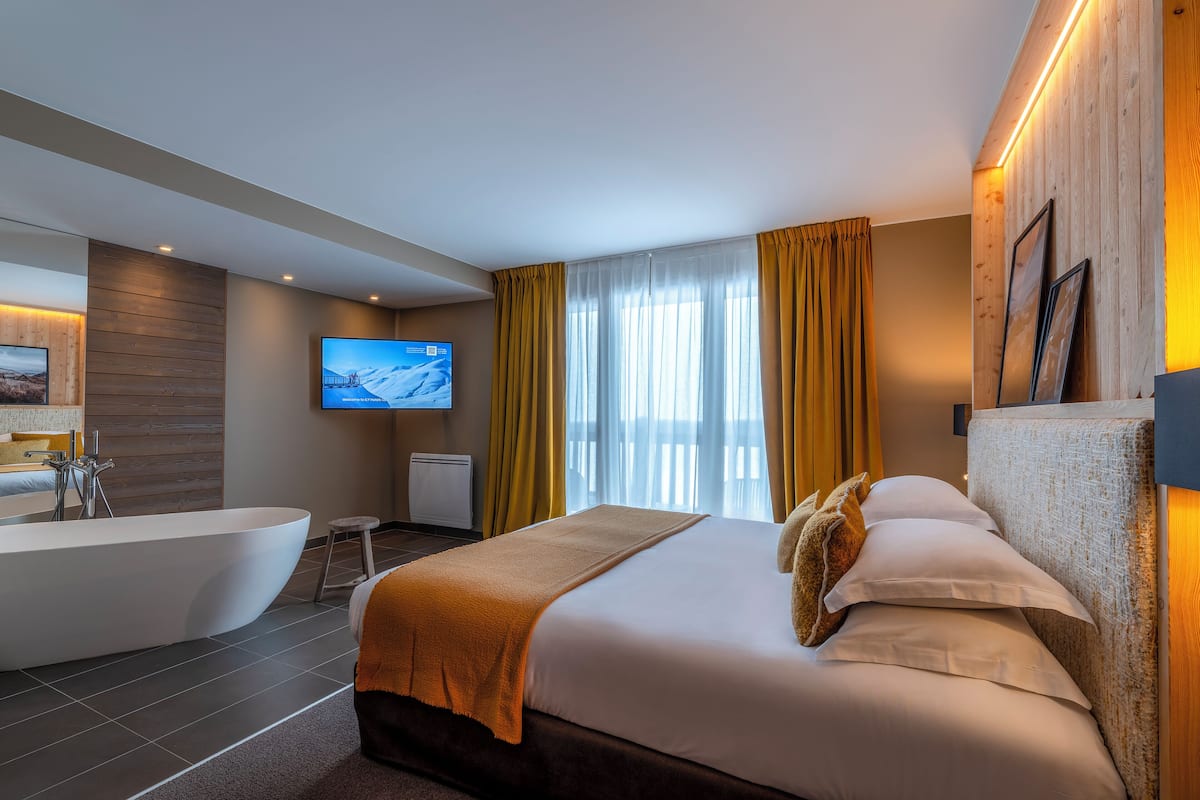 Ein modernes Hotelzimmer mit einem großen Bett, einer Badewanne, einem Flachbildfernseher und einer Wand mit Holzelementen.