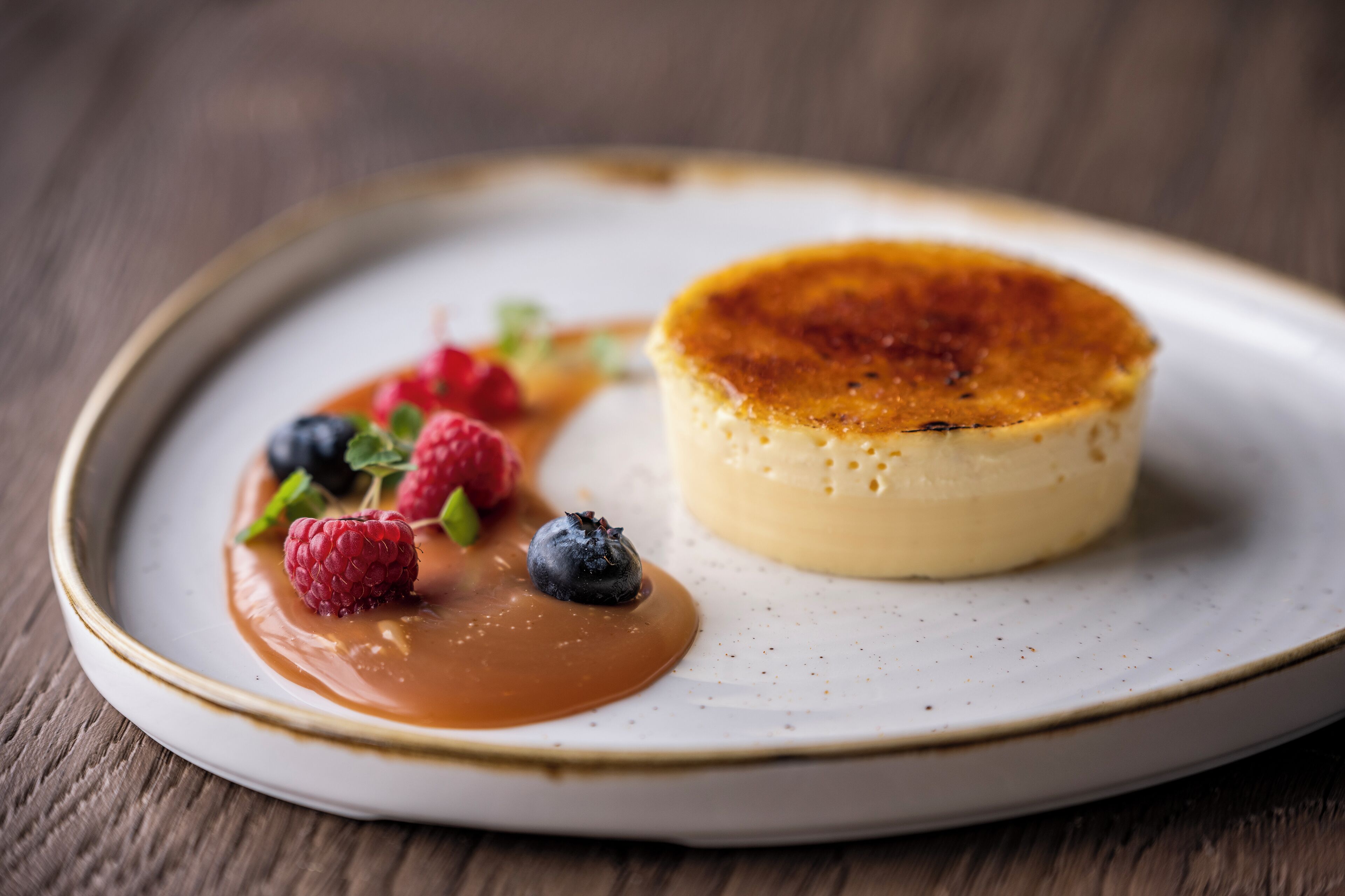 Un plato de postre con salsa de caramelo y frutos rojos.