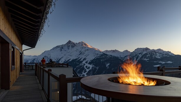 Una terraza de madera con un pozo de fuego y vistas a montañas nevadas.