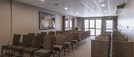 A conference room with rows of wicker chairs, a large framed picture on the wall, and a view through the door.