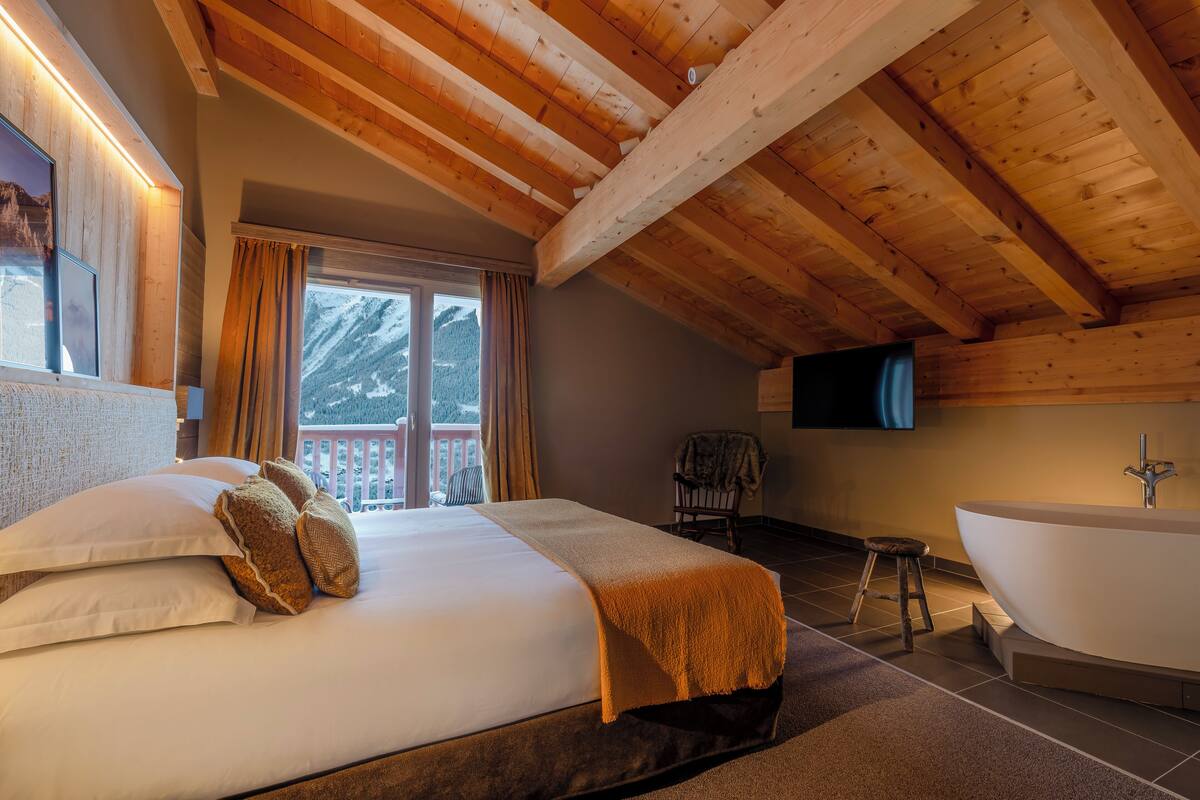 Ein Schlafzimmer mit einem großen Bett, einer Holzbalkendecke, einer Badewanne und einem Fernseher an der Wand.