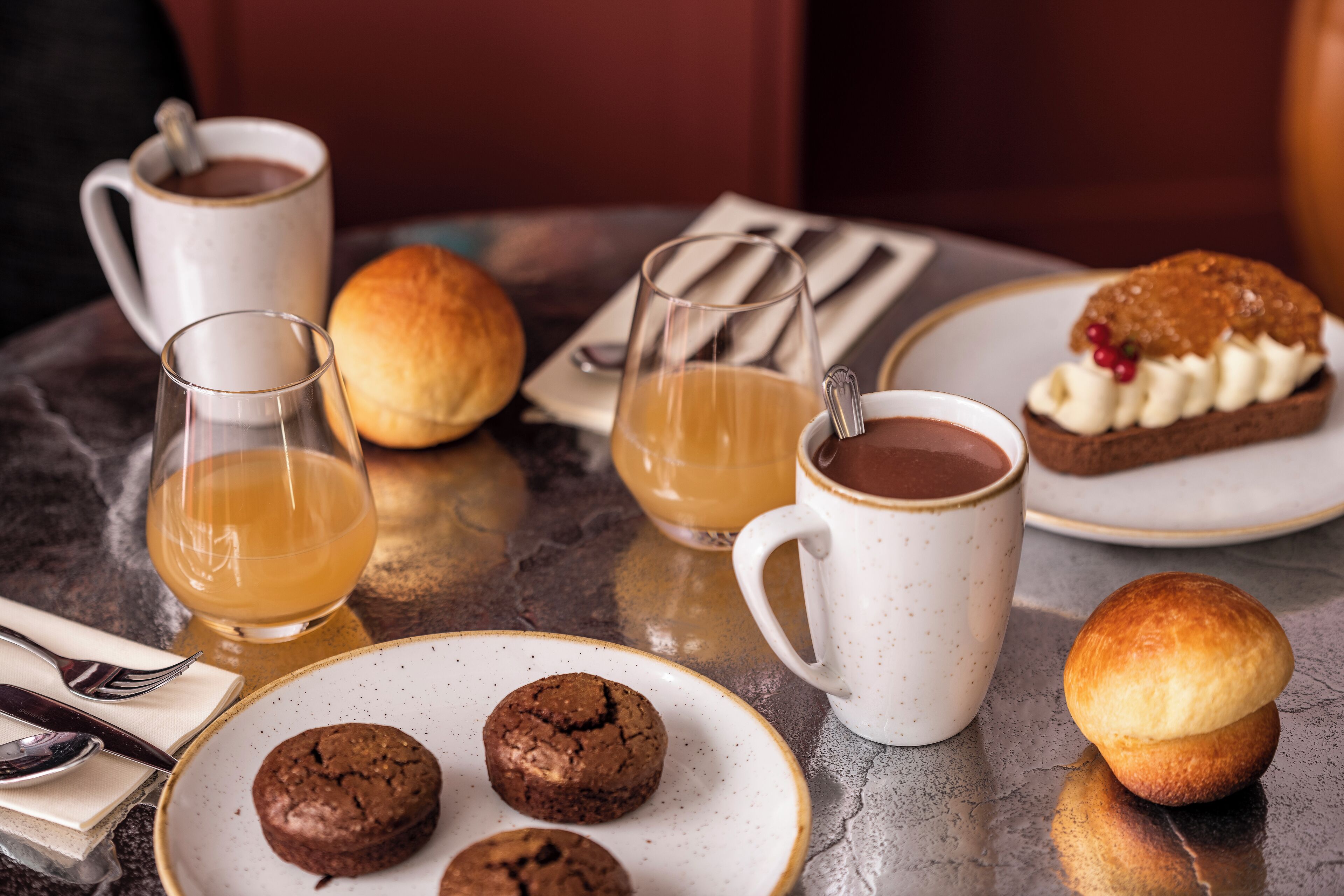A table with a variety of food items including cookies, a muffin, and a dessert with whipped cream and berries. There are also two cups of coffee and a glass of juice.