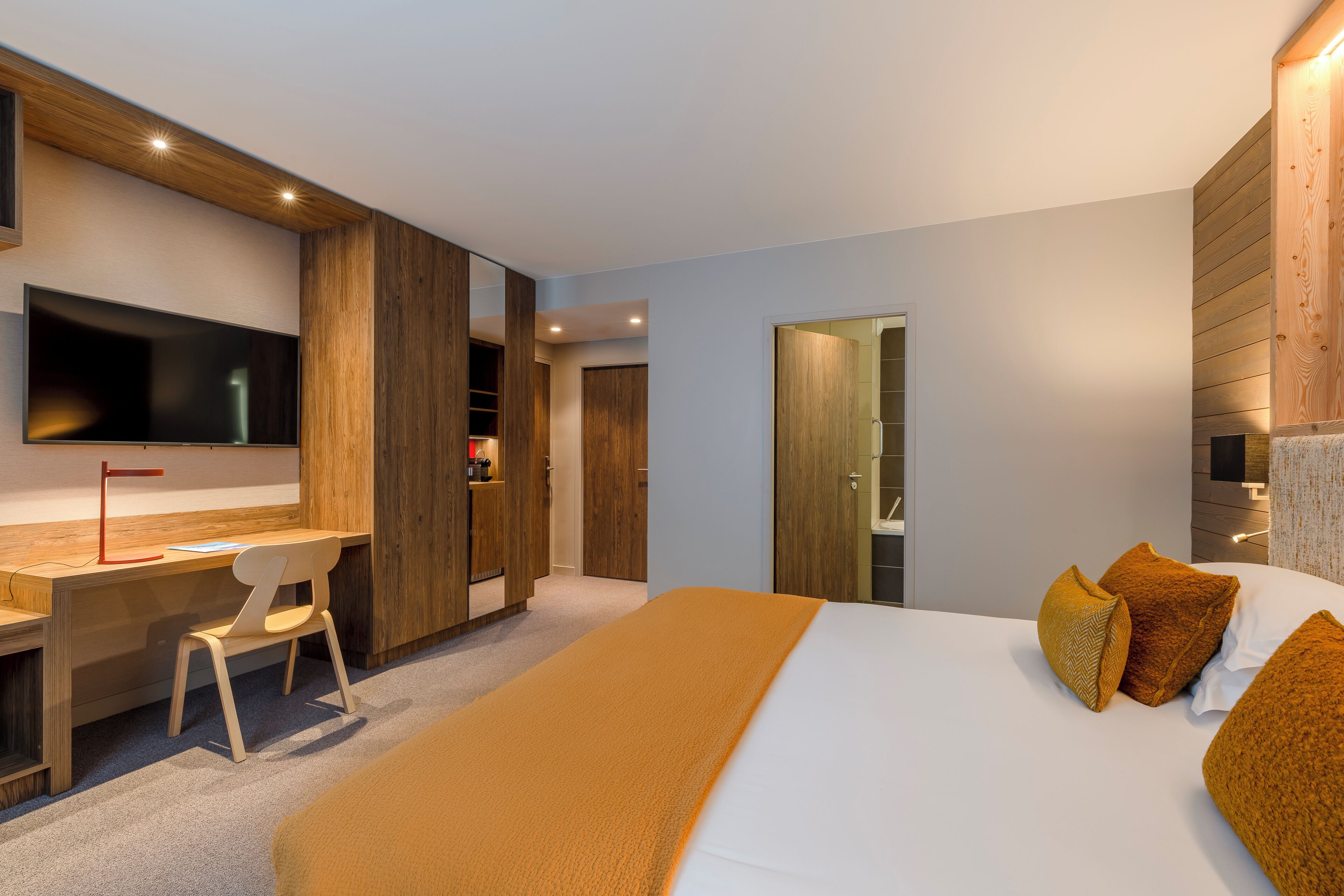 A modern hotel room with a large bed, a desk, and a TV.