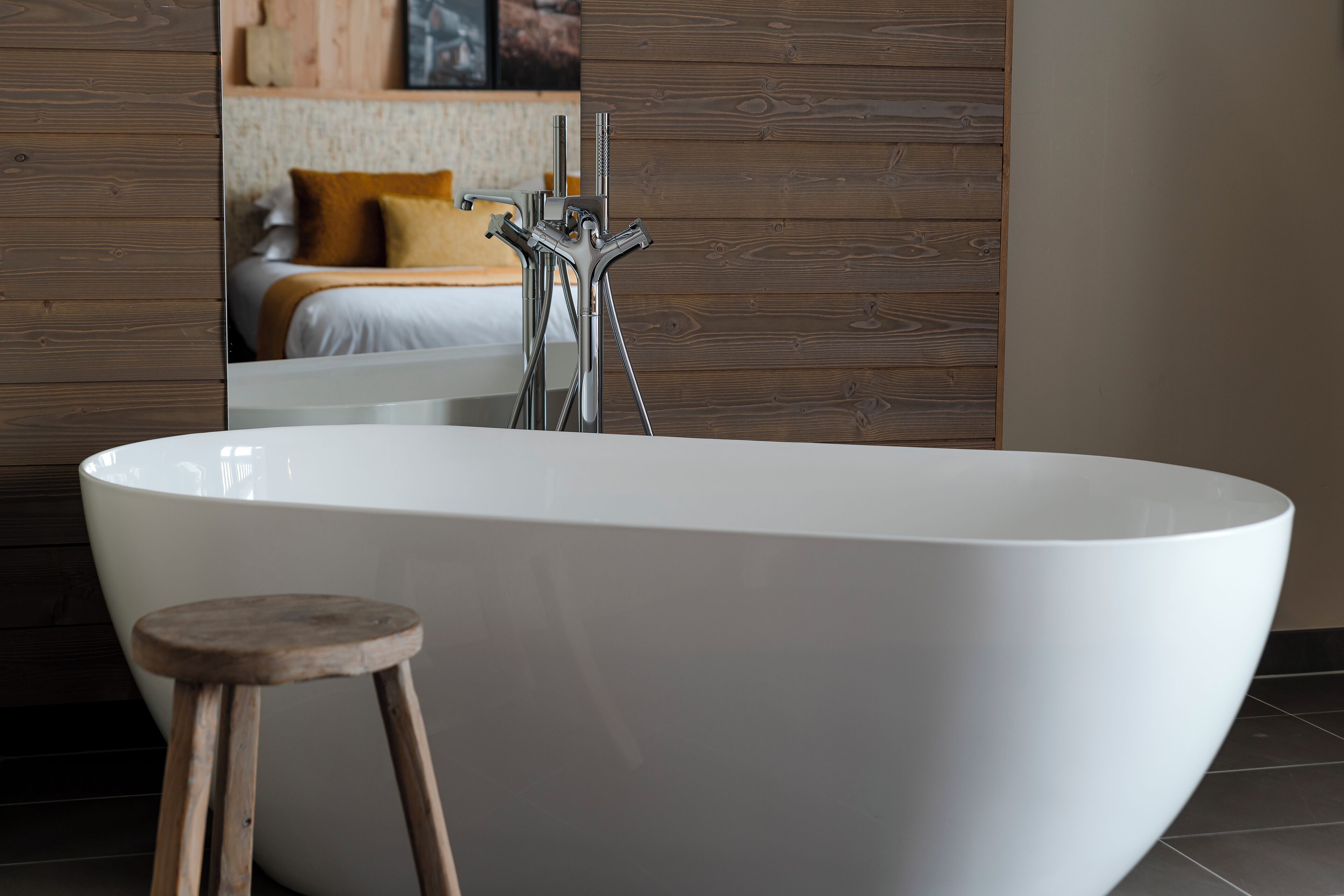 A modern bathroom with a freestanding bathtub, wooden stool, and a wooden wall panel.