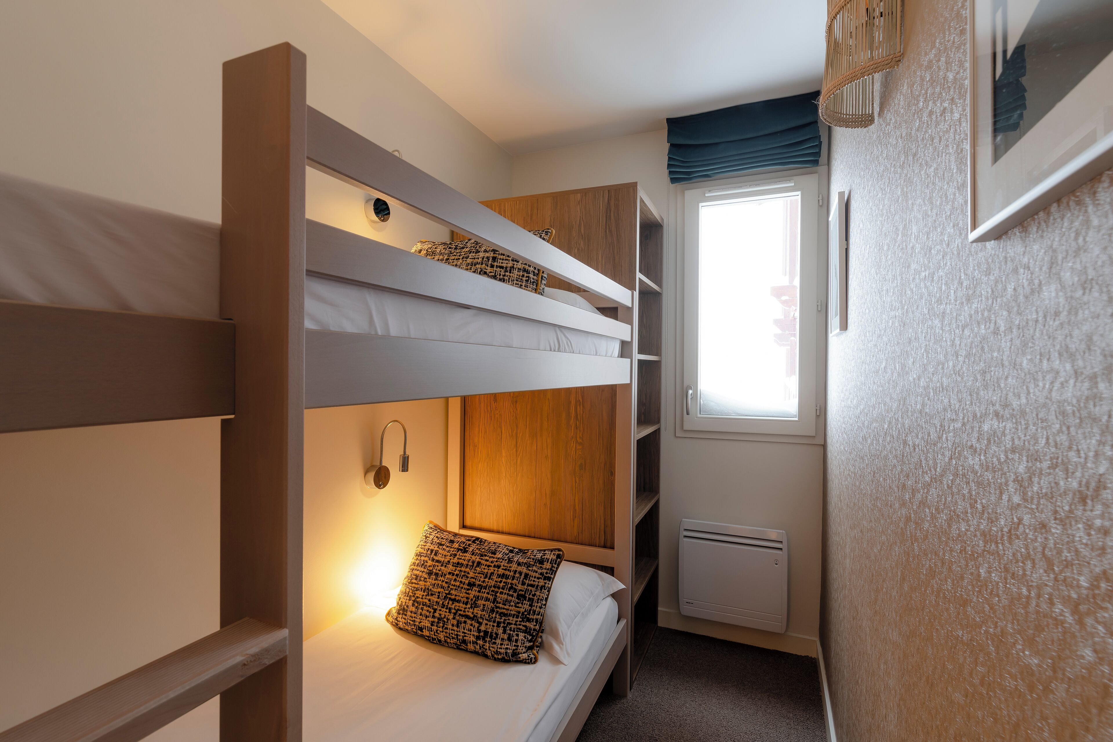 A bunk bed room with a window, a wall-mounted shelf, and a small cabinet.
