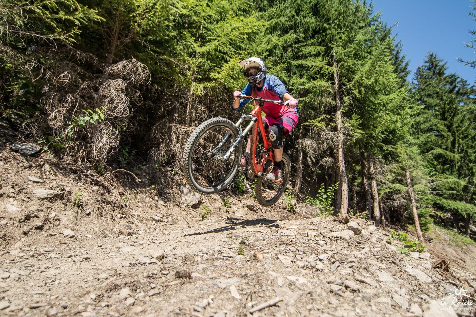 Un ciclista de montaña en un sendero pedregoso, rodeado de un bosque denso.