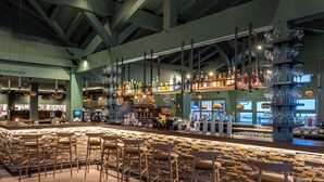 Un área de bar con paredes de piedra, taburetes de madera y estantes llenos de botellas y vasos.