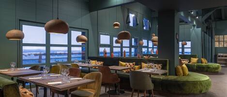 Un restaurante con mesas y sillas, ventanas amplias y vista al agua.