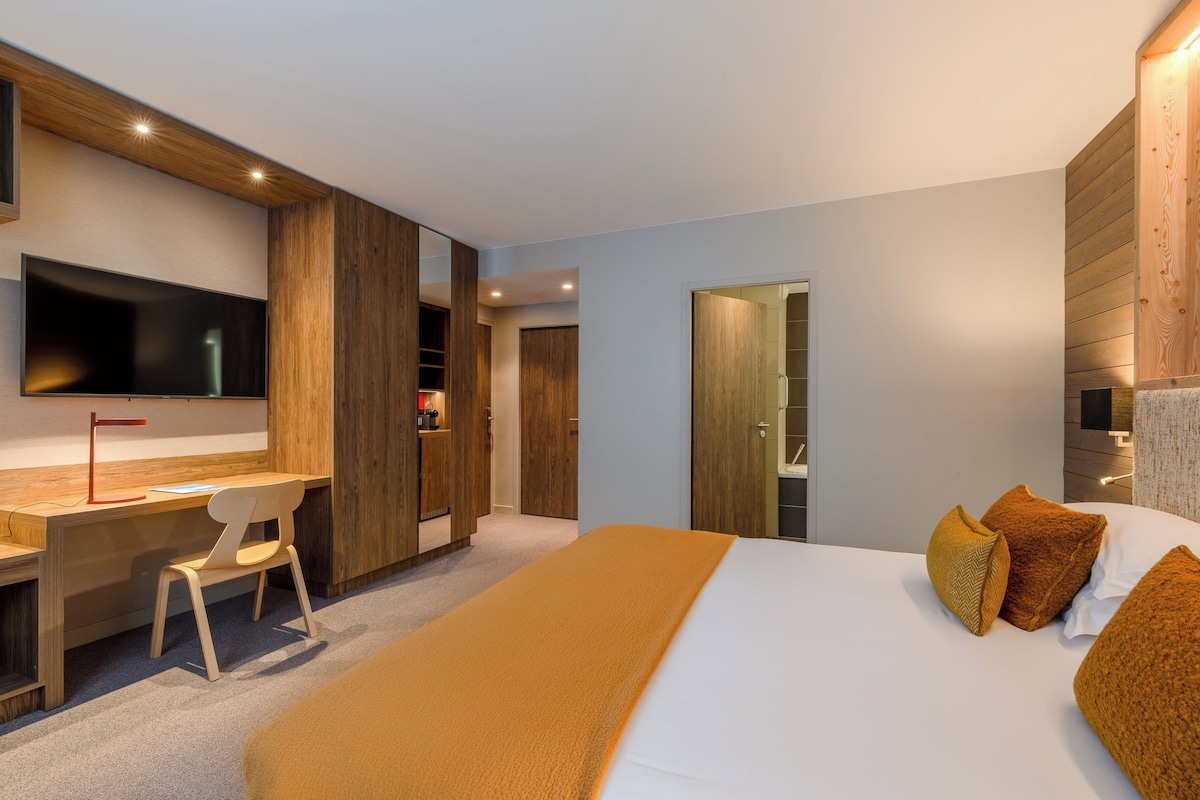 Une chambre d’hôtel moderne équipée d’un grand lit, d’un bureau, d’une chaise, d’une télévision et d’une armoire.