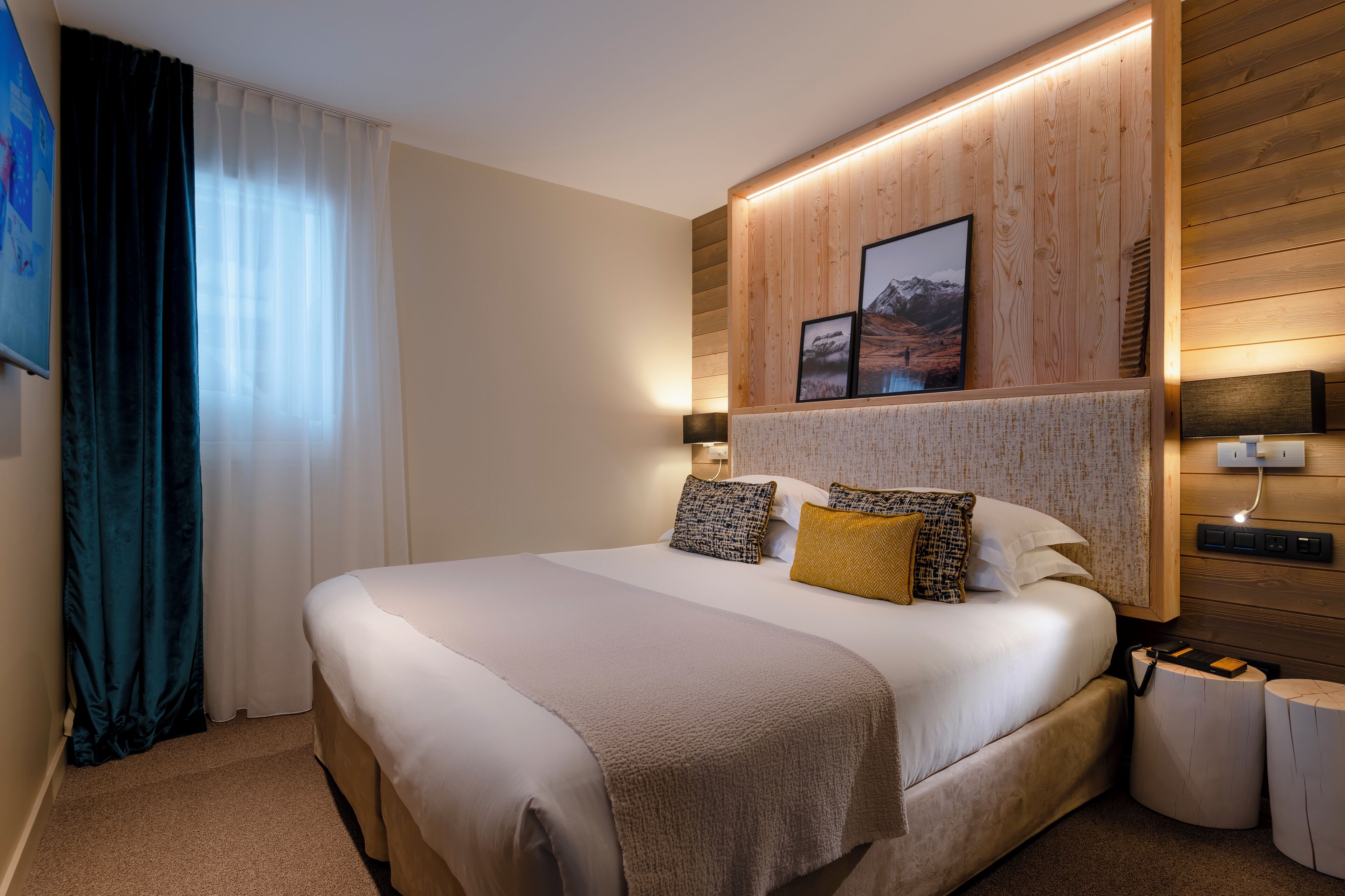 A hotel room with a large bed, wooden headboard, two bedside tables, and a wall-mounted TV.