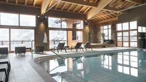 Una amplia piscina interior con vigas de madera, ventanas grandes y sillones de descanso.