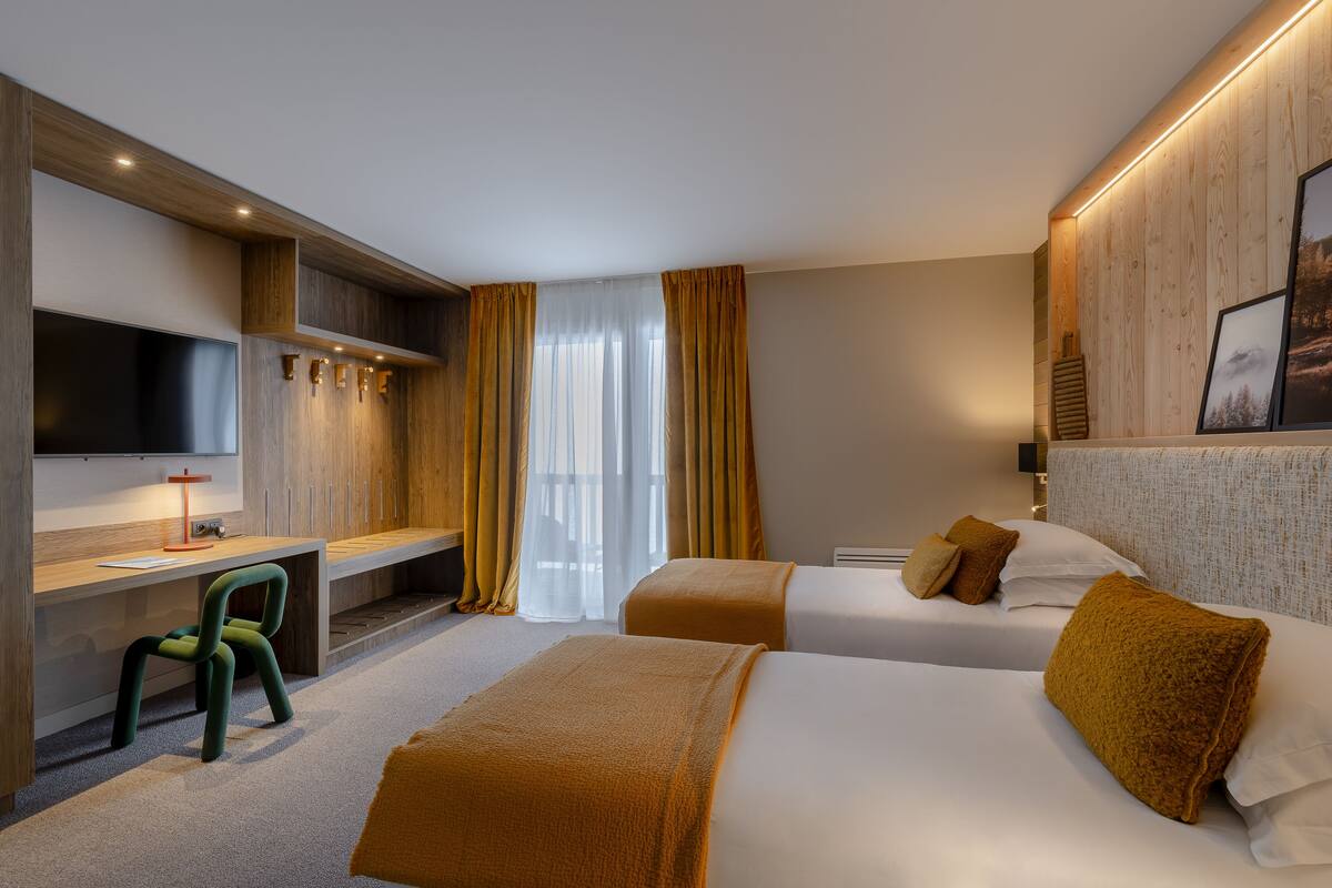Ein Hotelzimmer mit zwei Betten, einem Schreibtisch, einem Fernseher und einem Sessel.