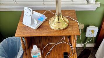 A wooden nightstand with a lamp, a white device, and a trash bin.