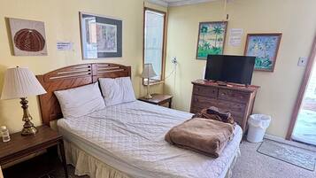 Una habitación de hotel con cama, ventilador de techo, televisor y obras de arte en las paredes.