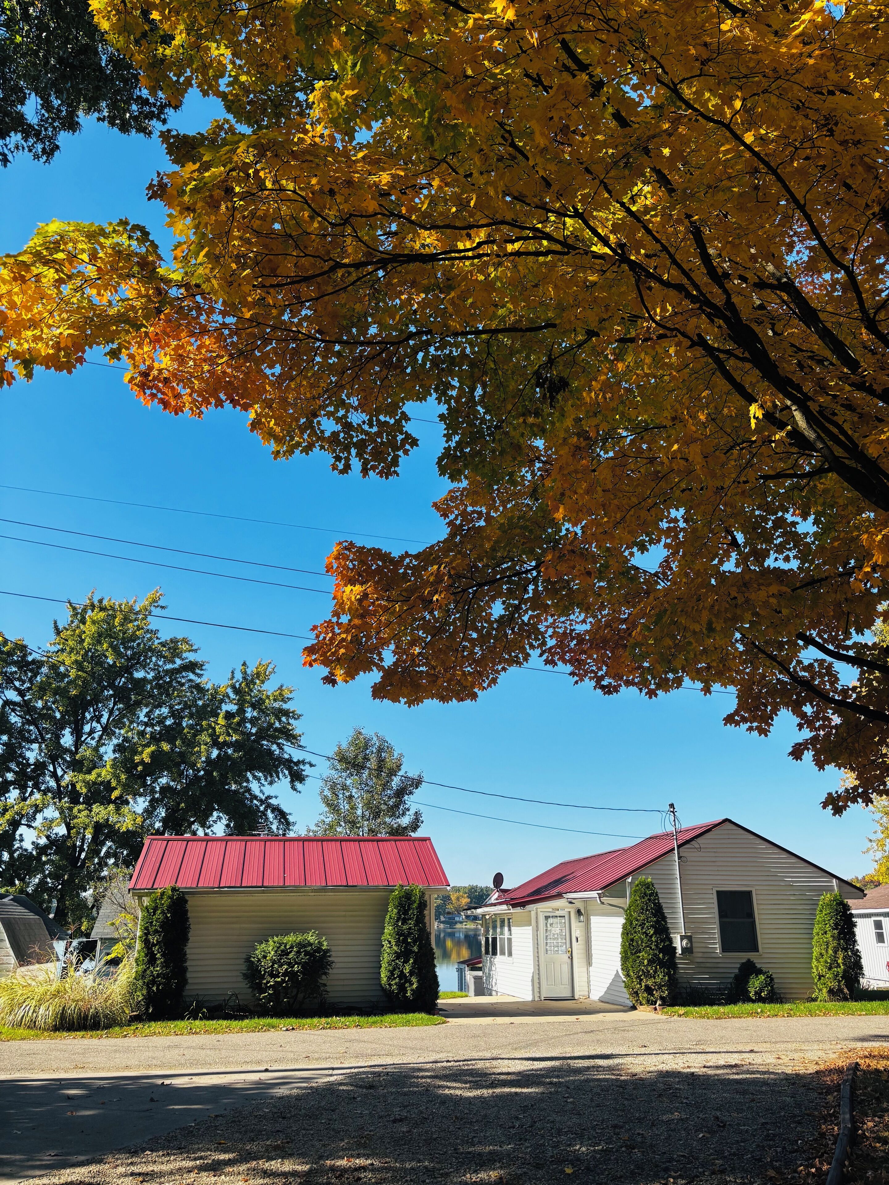 Une maison à deux étages avec un toit rouge, entourée d’arbres aux feuilles d’automne.