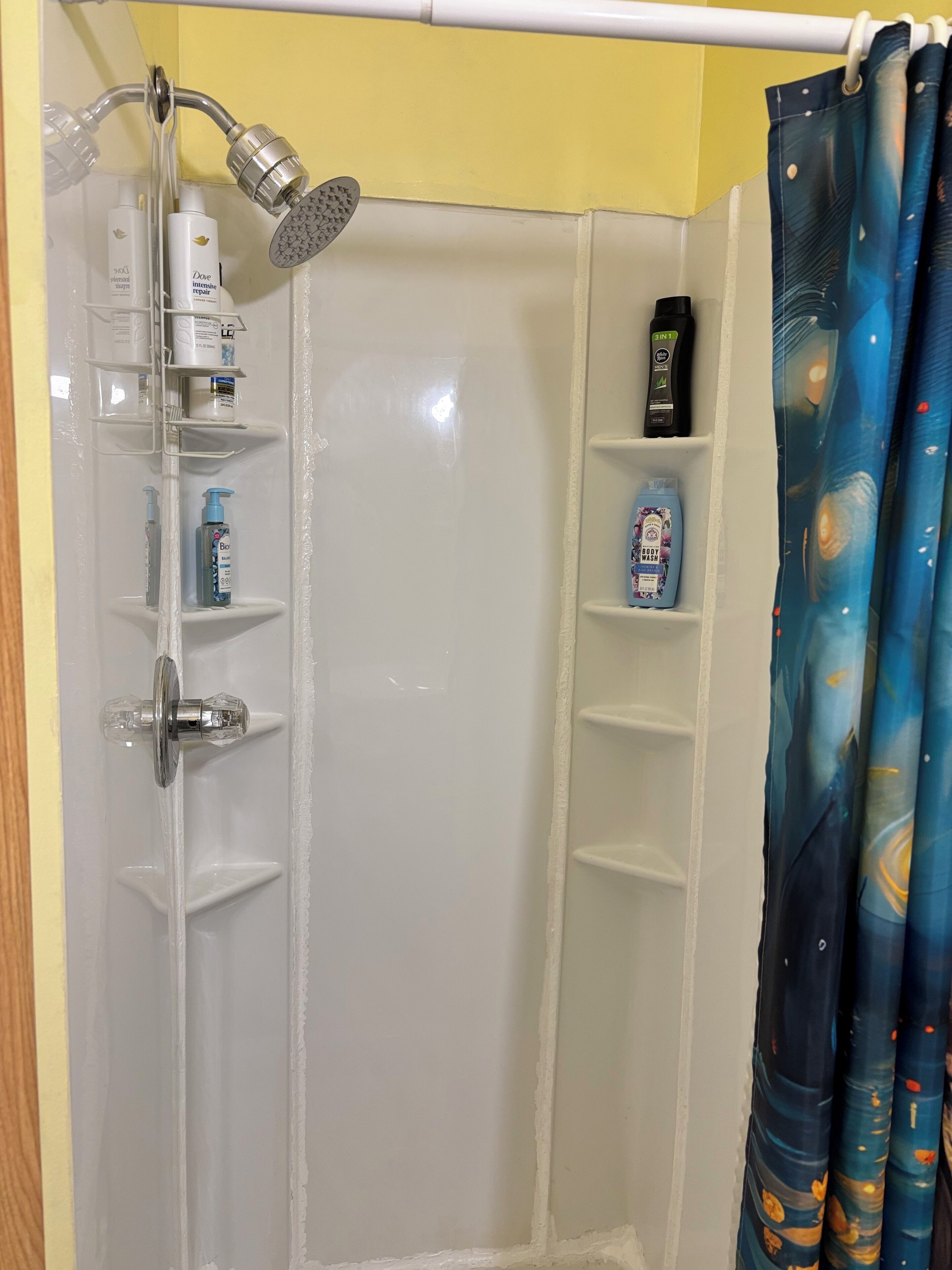 A shower area with a glass enclosure, a handheld showerhead, and shelves with toiletries.