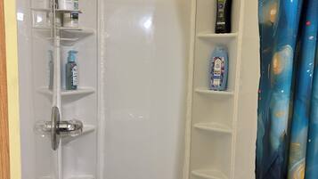 A shower area with a glass enclosure, a handheld showerhead, and shelves with toiletries.