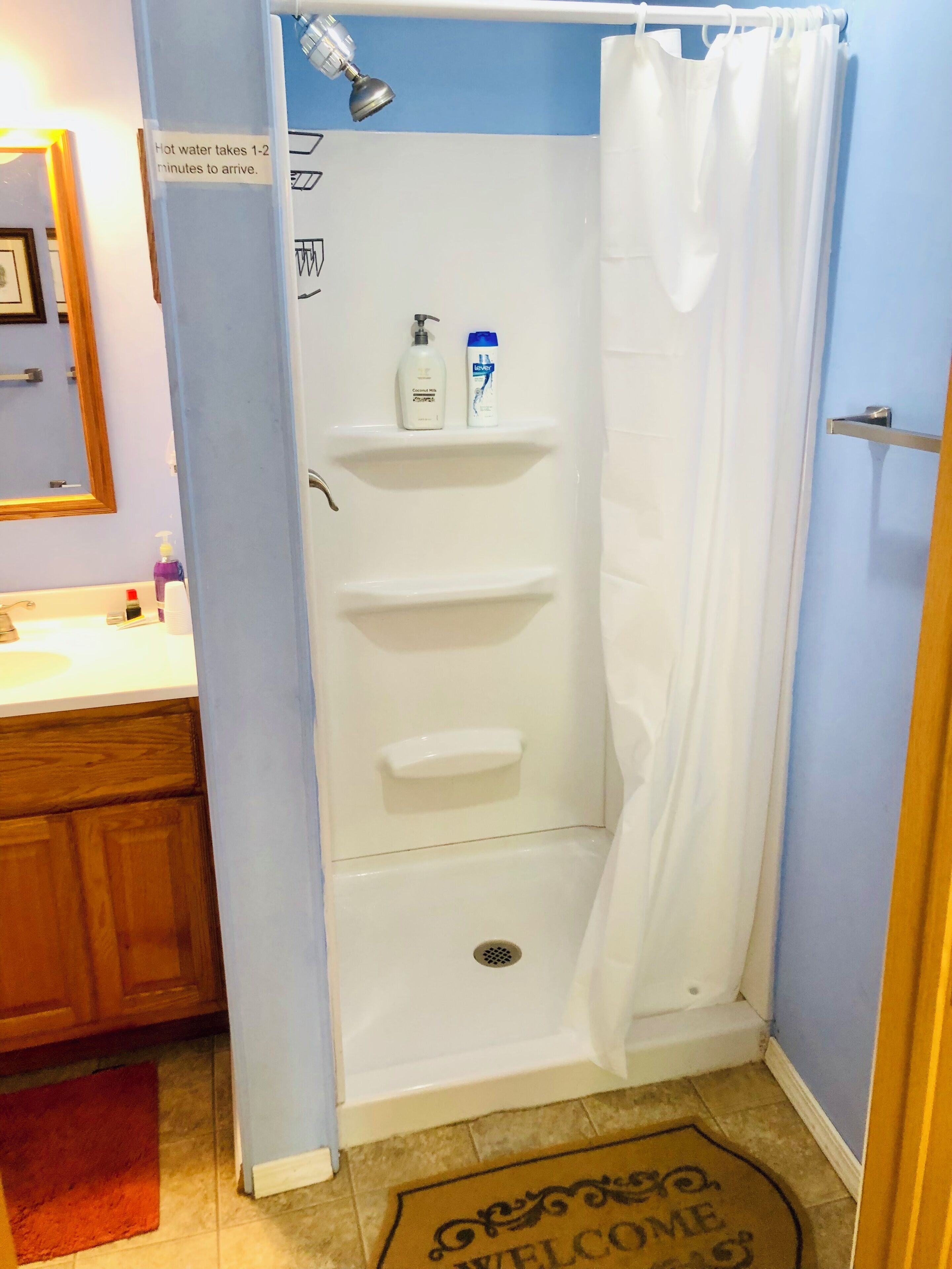 A bathroom with a shower, a sink, and a toilet. There is a sign indicating hot water takes 1-2 minutes to arrive.