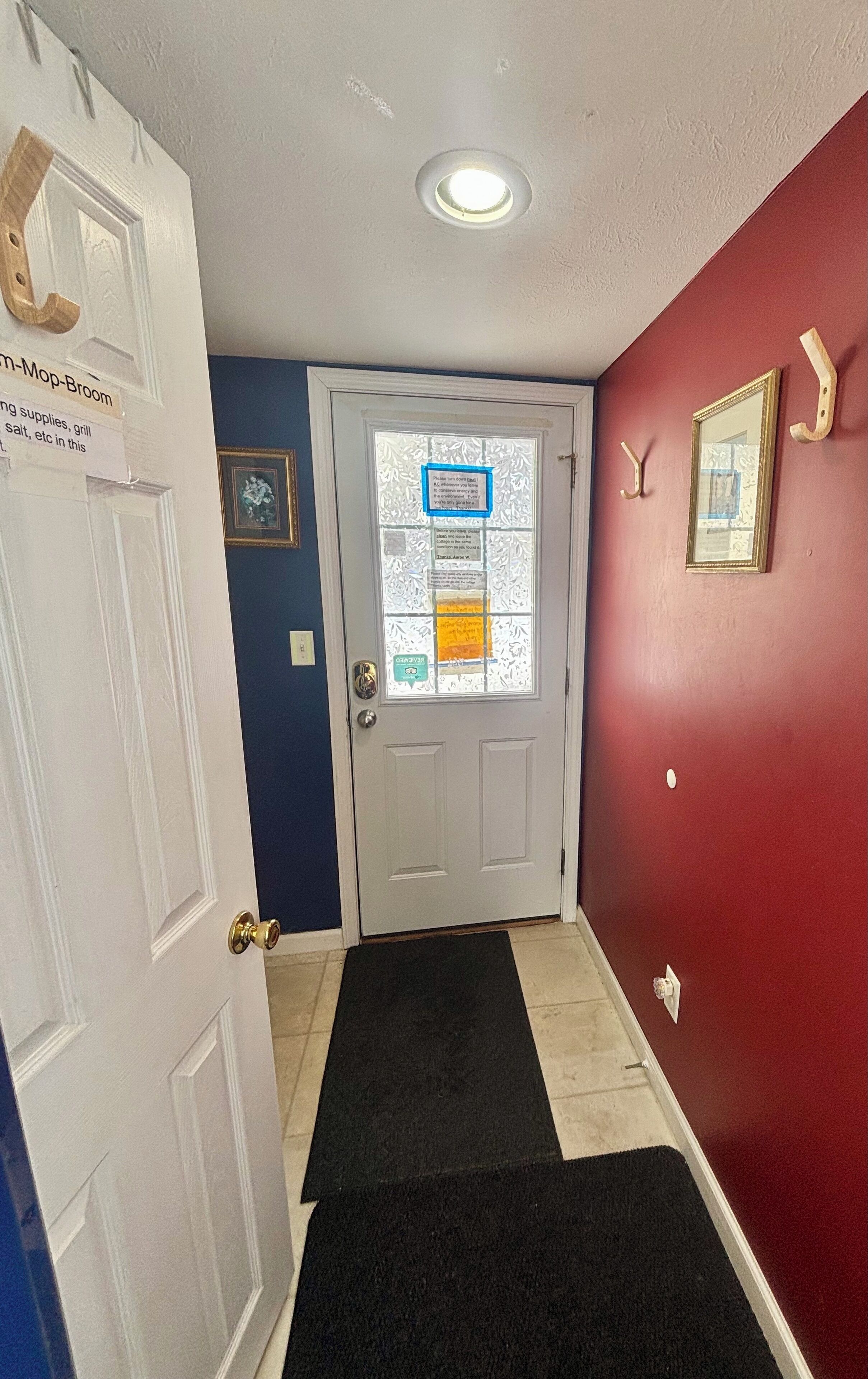 A hallway with a white door, a black doormat, a red wall, and a ceiling light.