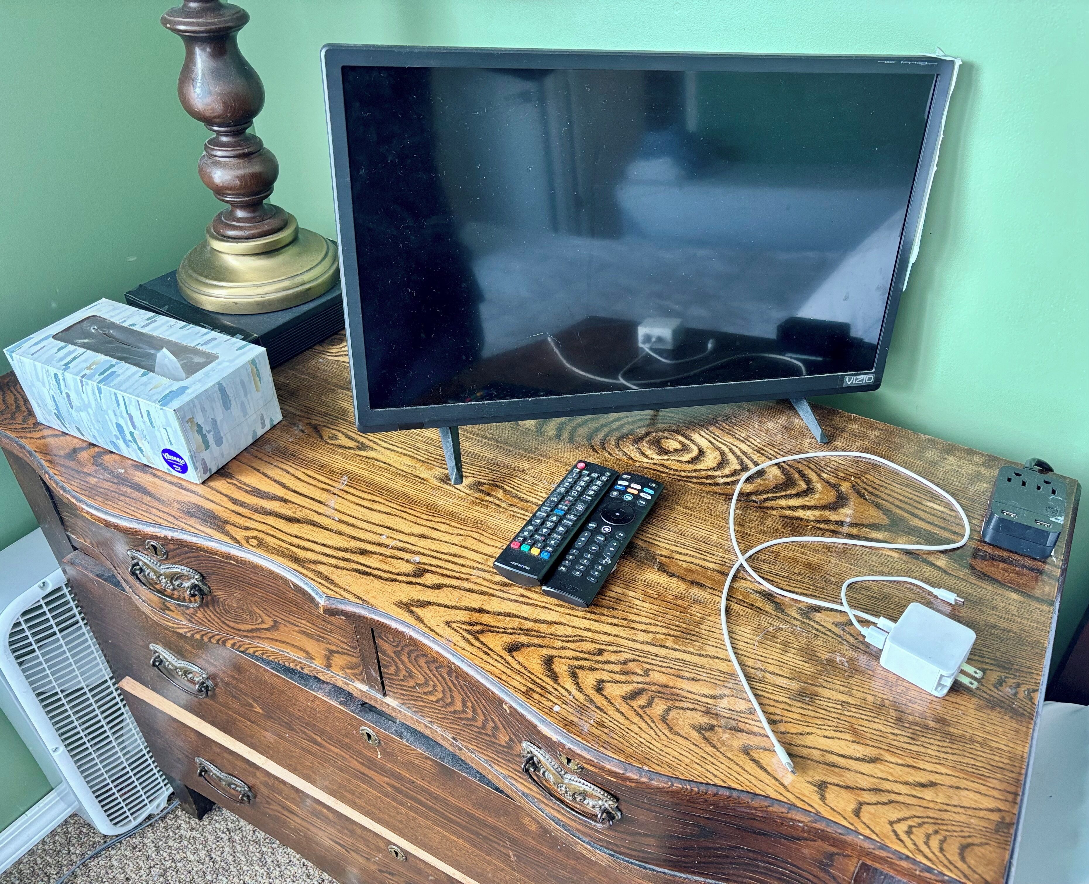 A wooden dresser with a television, remote controls, and a power strip.