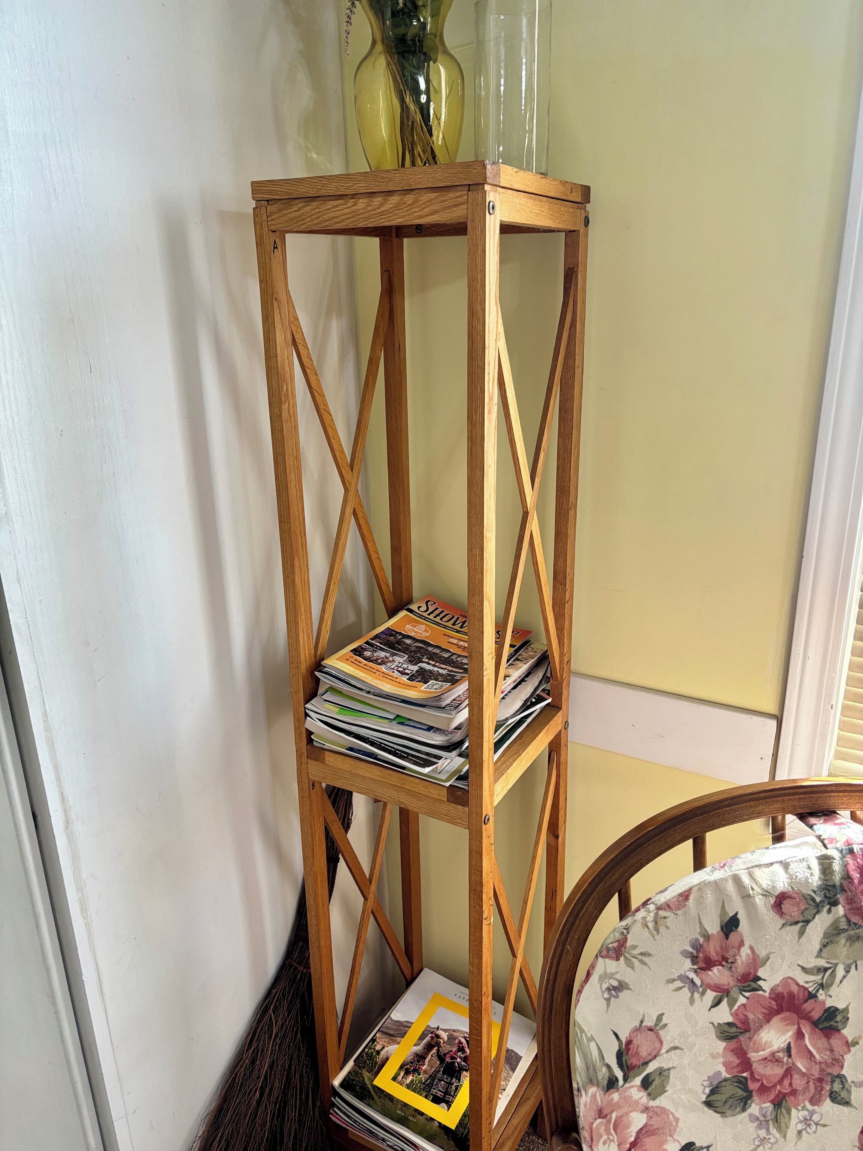 Een houten boekenkast met tijdschriften en een vaas erop.