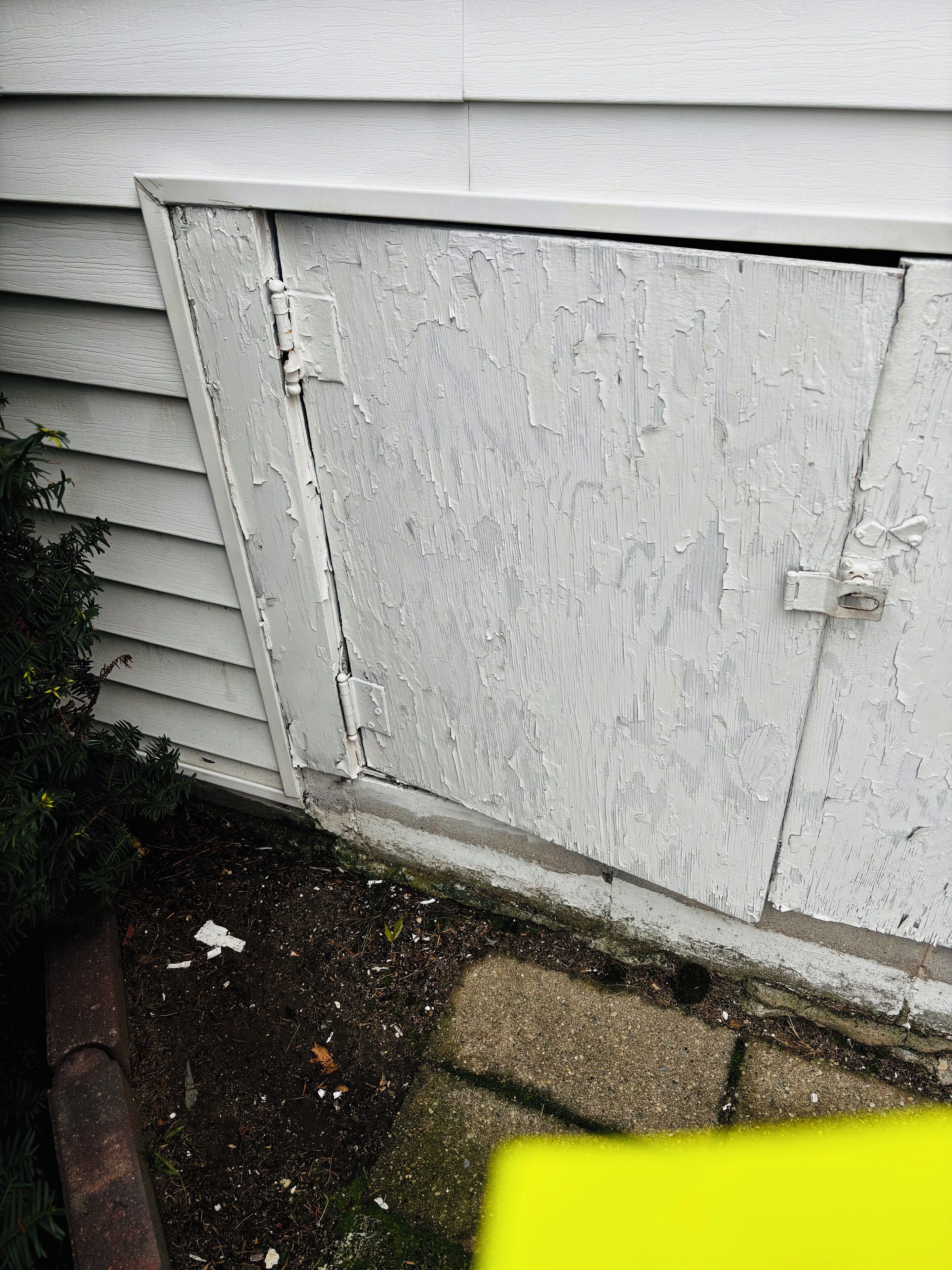A white exterior wall with peeling paint and a visible door latch.