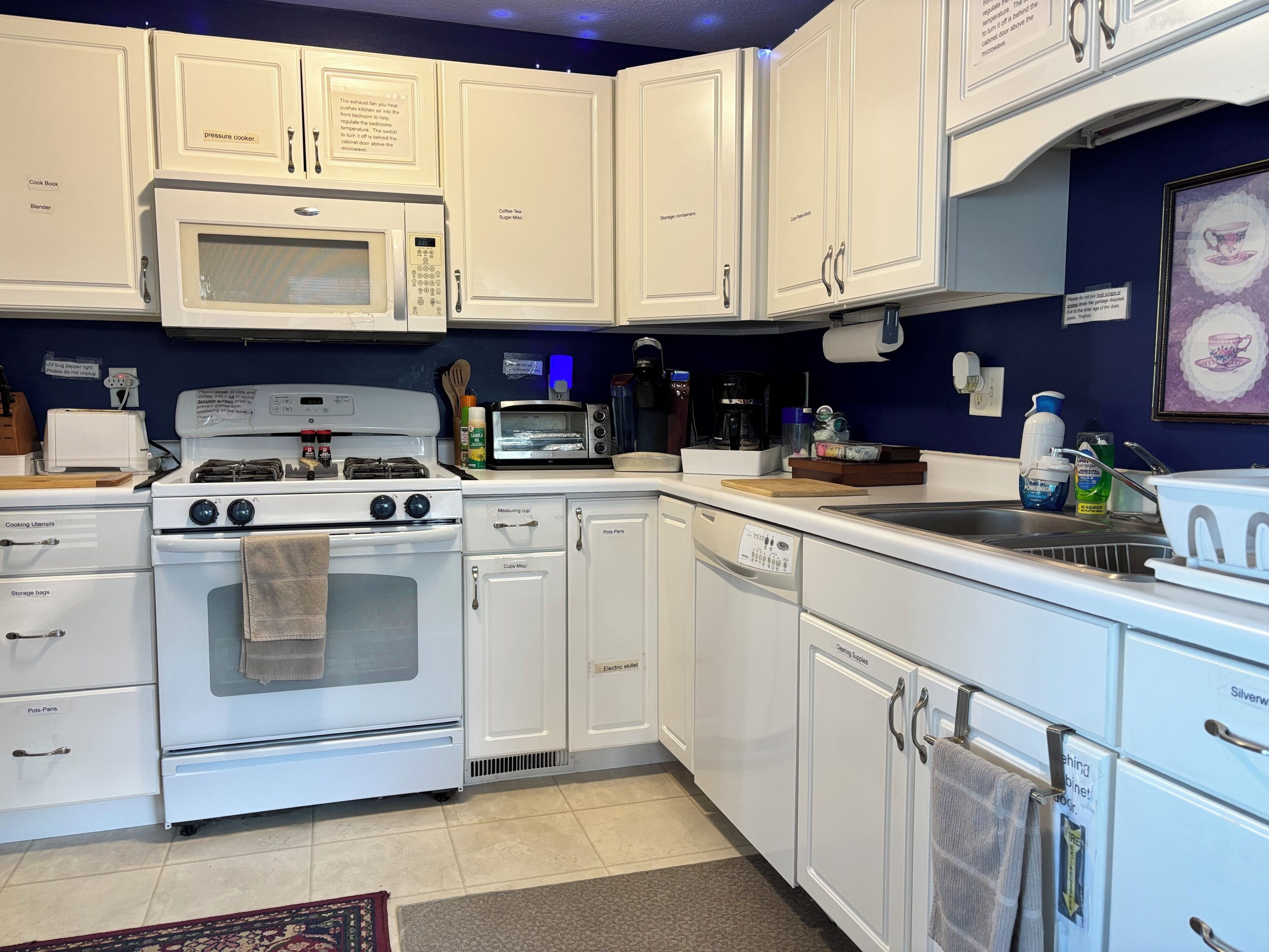 Cocina con gabinetes blancos, microondas, estufa, horno y un lavabo.