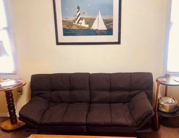 A dark-colored sofa in a living room with a framed picture of a lighthouse and sailboat on the wall. - The Wellington Cottage (Middlebury)