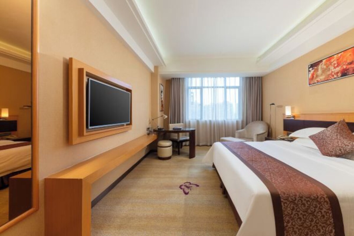 Una habitación de hotel con una cama grande, un escritorio, una silla, un televisor y una ventana con cortinas.