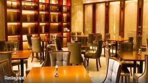 Un restaurante con varias mesas y sillas, una pared iluminada con botellas y una iluminación interior cálida.