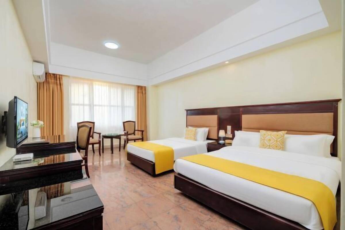 Habitació d'hotel amb dos llits, un escriptori amb un ordinador, una televisió i una finestra amb cortines.