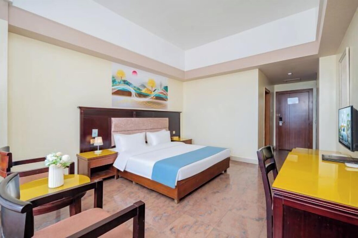 A hotel room with a bed, a desk, a chair, a TV, and a painting on the wall.