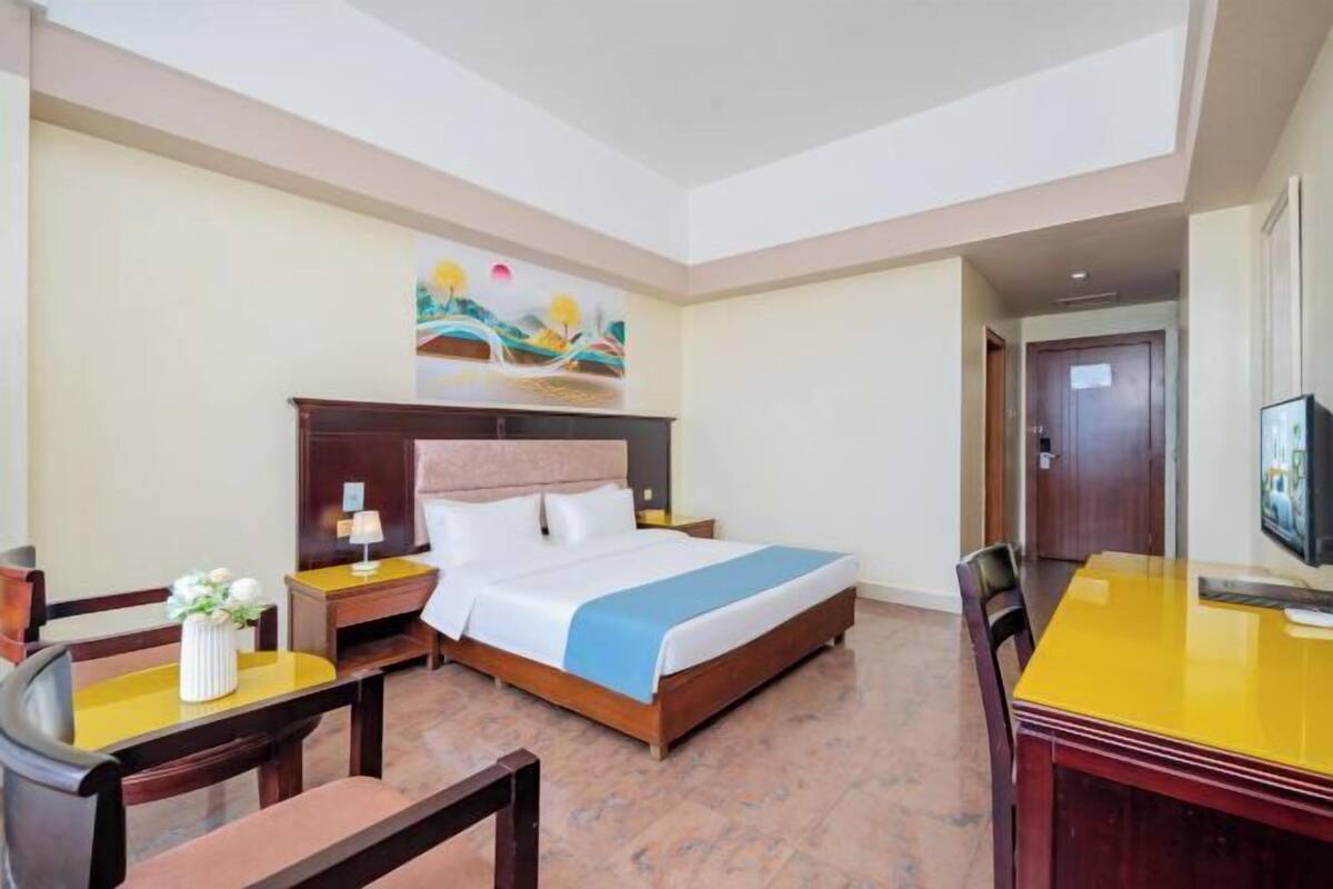 Una habitació d'hotel amb llit, escriptori, cadira, televisió i un quadre a la paret.