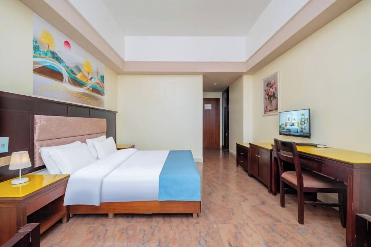 Une chambre d’hôtel équipée d’un lit, d’une table de chevet, d’un bureau, d’une chaise, d’une télévision et d’œuvres d’art accrochées aux murs.