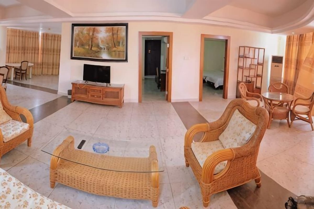 A spacious living room with wicker furniture, a flat-screen TV, and a dining area with chairs and a table.