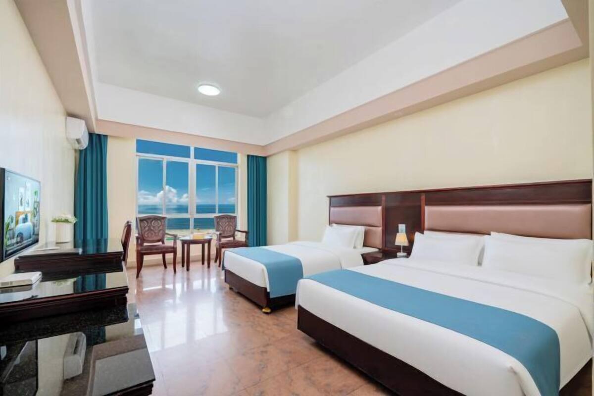 Habitació d'hotel amb dos llits, una escriptori, una cadira, un televisor i vista al mar.