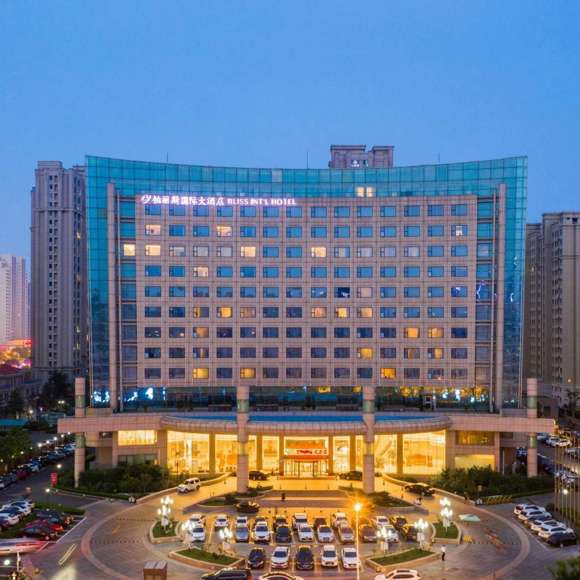 A multi-story hotel with a modern glass facade, a central entrance, and a parking lot.