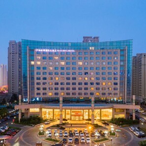 A multi-story hotel with a modern glass facade, a central entrance, and a parking lot.