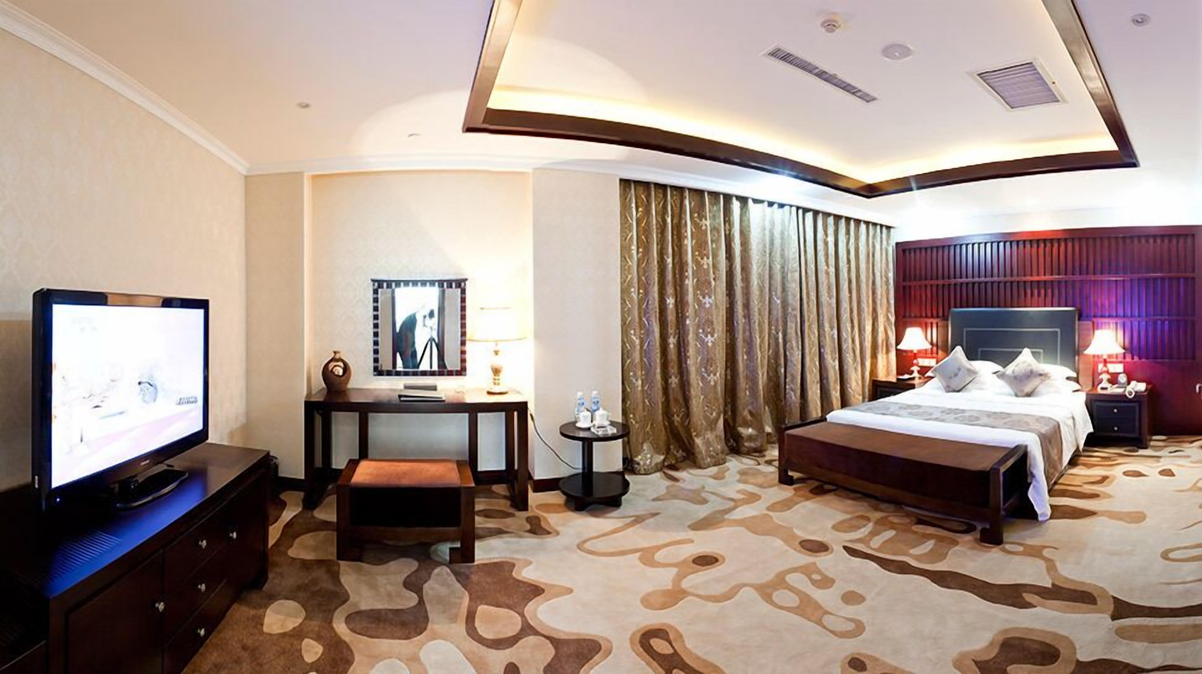 A hotel room with a television, desk, chair, bed, and curtains.