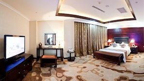 A hotel room with a television, desk, chair, bed, and curtains.