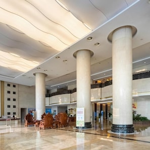 A spacious lobby with large columns, a reception desk, and a seating area with ornate chairs.