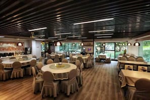 Un restaurante con mesas y sillas redondas, piso de madera e iluminación colgante.