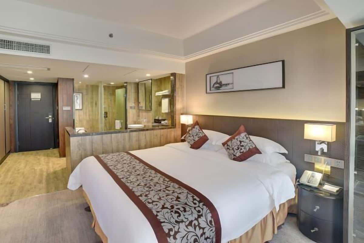 A hotel room with a large bed, bedside lamps, a mirror, and a framed picture on the wall.