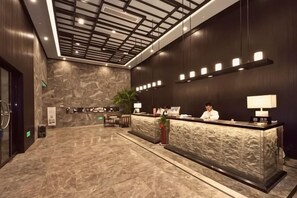 Zona de recepción de hotel con piso de mármol, mostrador de recepción, recepcionista y diseño moderno de techo.