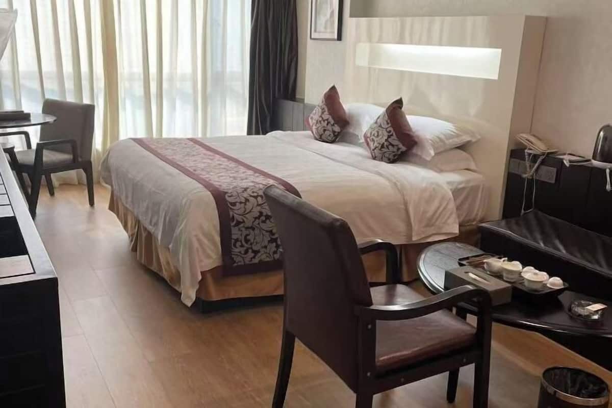 A hotel room with a bed, a desk, a chair, and a small table with a tray of items.