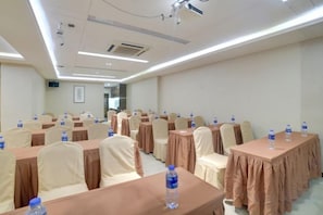 Una sala de conferencias con filas de mesas y sillas, cada una con mantel y una botella de agua encima.
