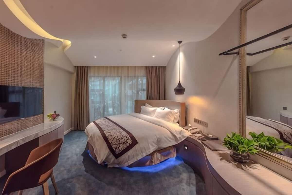 A hotel room with a bed, desk, chair, and a large mirror.
